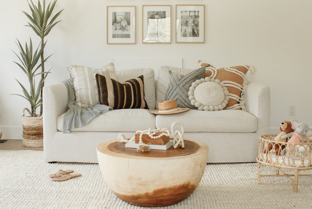 Un coin confortable composé d'un canapé beige rempli de coussins, une plante, des photos encadrées au mur, une table basse et un tapis doux au sol.