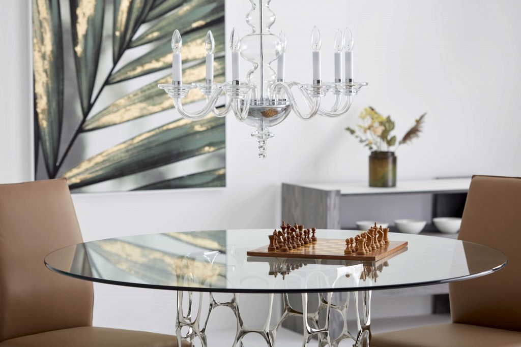 Salle à manger composée d'une petite table ronde en verre sur laquelle est disposé un jeu d'échecs. Au dessus de la table, une belle lampe suspendue façon chandelier.