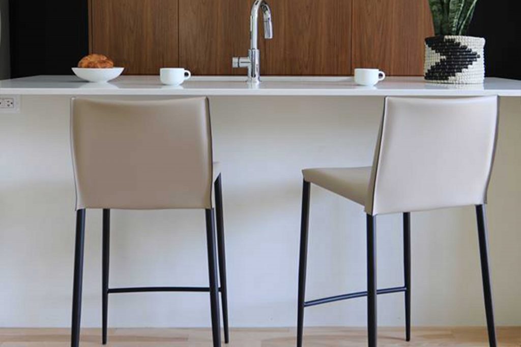 2 white leather stools with black legs in front a bar